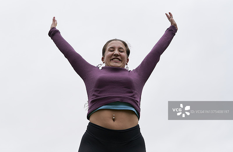 穿着运动服、肚脐穿孔的快乐跳跃的女人低角度视图图片素材