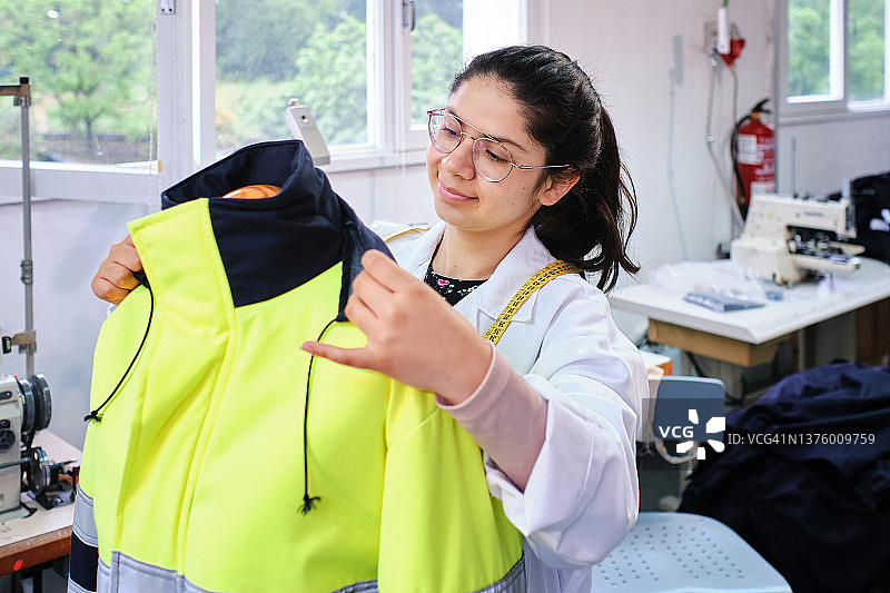 拉丁裔女裁缝在缝纫 workshop 里拿着特殊的工作夹克图片素材