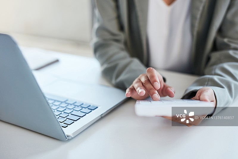 办公室里一位身份不明的女商人使用计算器和笔记本电脑的特写镜头图片素材