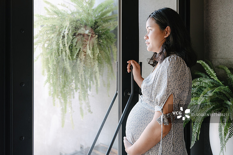 孕妇站在客厅门口抚摸肚子图片素材