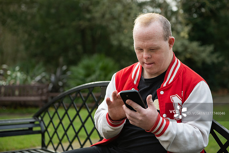 坐在长椅上使用手机的唐氏综合征男子图片素材