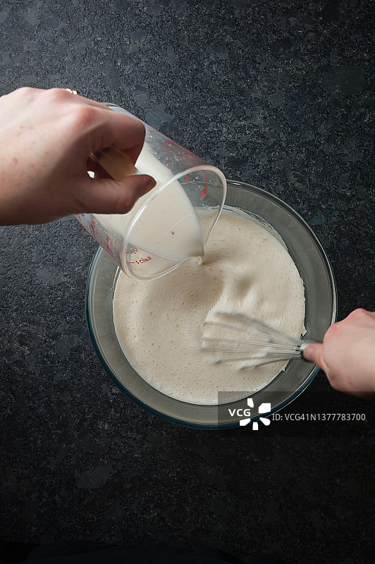 制作顺滑的蛋奶沙司，步骤2：将蛋黄和糖放入大玻璃碗中，倒入热牛奶并搅拌图片素材