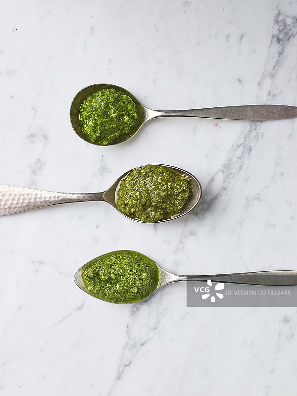 花岗岩背景上不同勺子里的各种意式香蒜酱：顶部到底部：烤干的坚果或种子、胡萝卜叶、欧芹茎图片素材