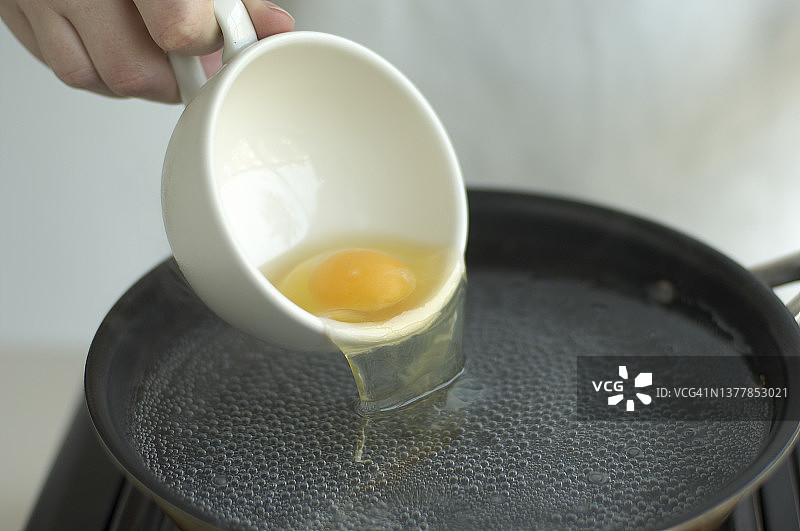 水波蛋：将生鸡蛋从茶杯倒入装有沸水的锅中图片素材