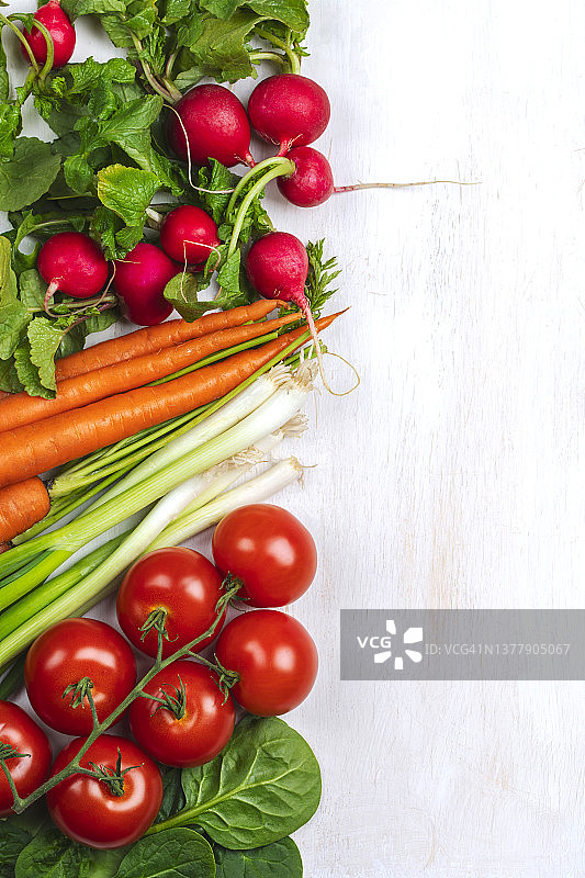 白色木质背景上的新鲜胡萝卜、萝卜、西红柿和葱，框架，顶部视角，留白图片素材