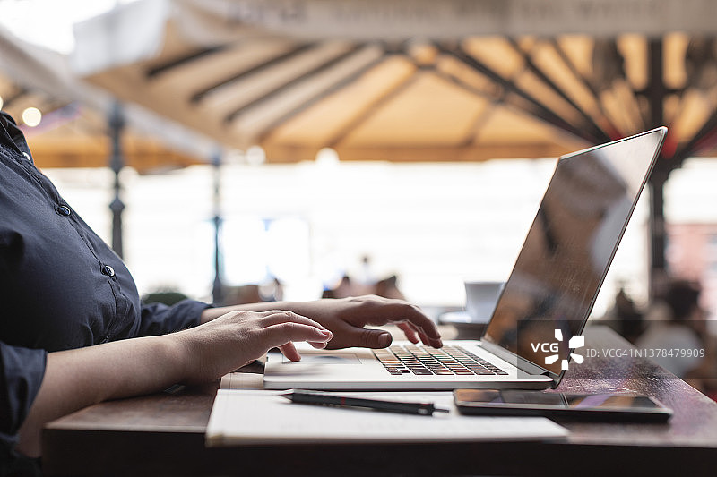 大码女人在人行道咖啡馆一边喝咖啡一边在笔记本电脑上写博客图片素材