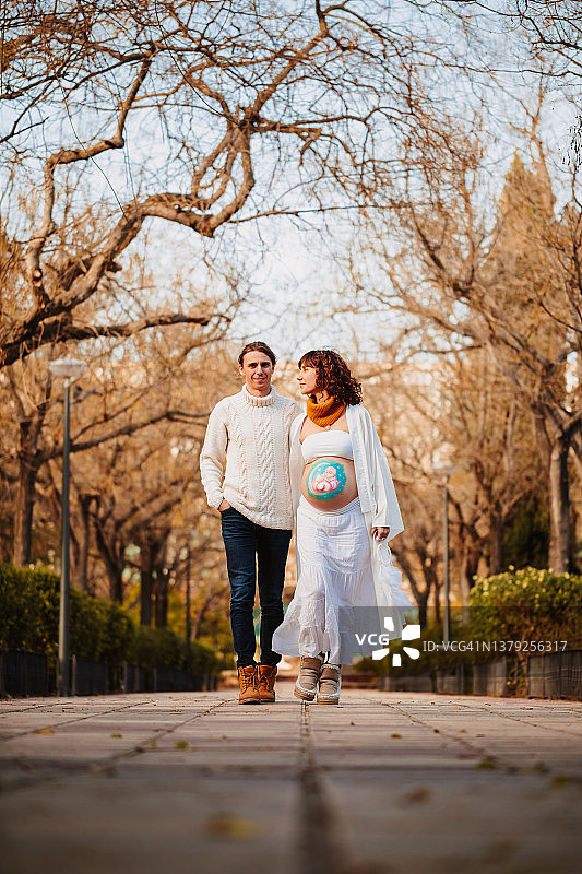 艺术彩绘腹部的孕妇与准爸爸在公园里散步图片素材