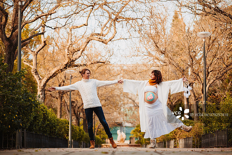 腹部绘有婴儿曼陀罗图案，与准爸爸在公园里跳舞的孕妇图片素材