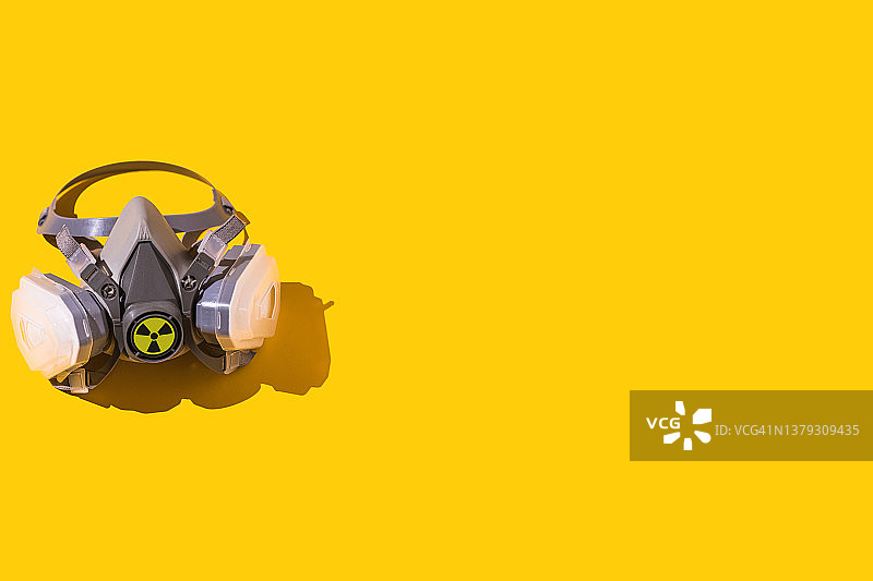带有核标志的防护口罩，位于黄色背景的左侧。核能、能源、供应、灾难、对抗、化学武器、危险和切尔诺贝利的概念图片素材