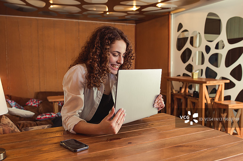 红发卷发女孩在家用电脑工作。学生使用笔记本电脑。享受工作，庆祝胜利，事业有成图片素材