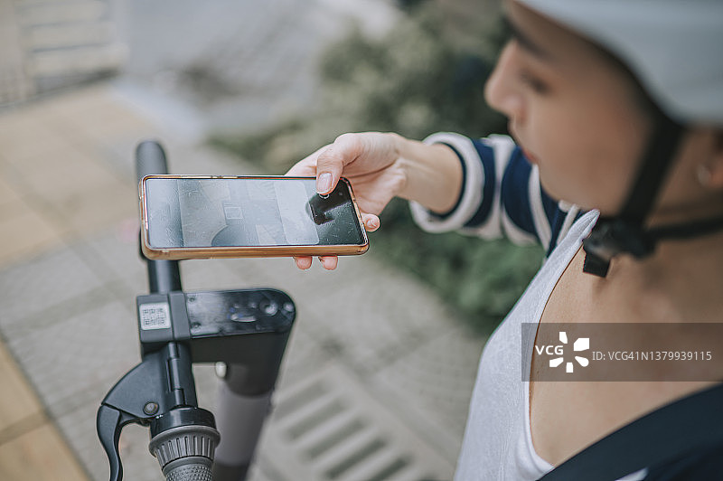 华人女性使用手机App解锁电动滑板车，用于城市通勤图片素材