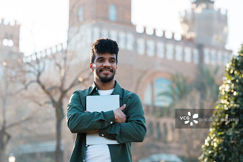 非洲裔男学生在大学校园户外手持笔记本电脑图片素材