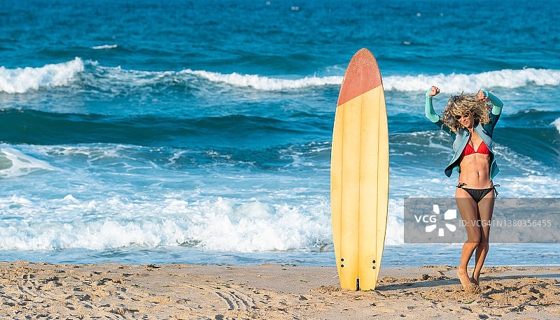 冲浪生活方式：年轻金发女子身穿比基尼，在海滩上拿着冲浪板图片素材