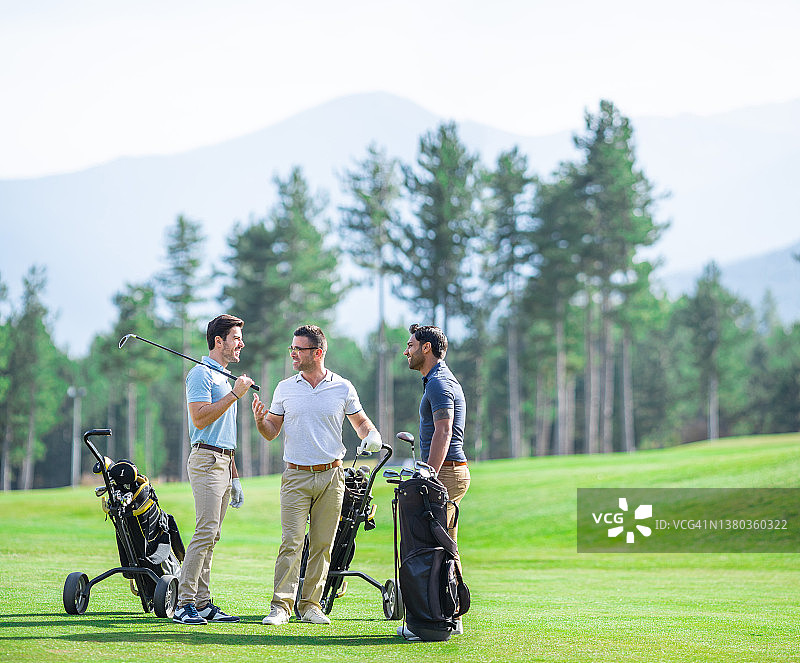 一群男性高尔夫球友在阳光明媚的日子里打高尔夫，在球场上交谈微笑图片素材