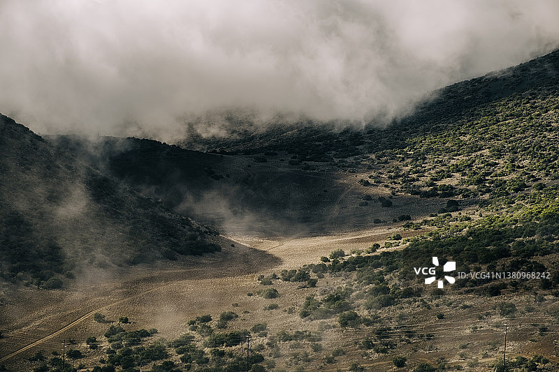山谷中蜿蜒土路的航拍，前景是低矮的云层图片素材