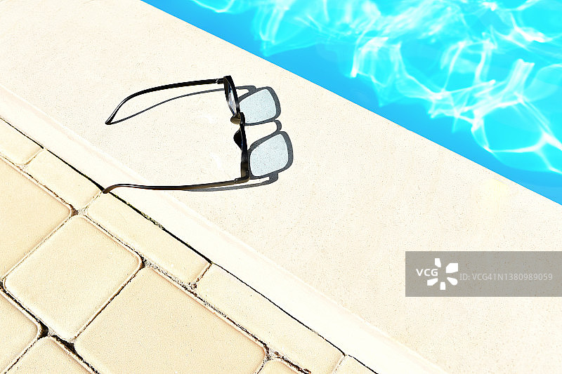 泳池边的太阳镜。游泳池。炎热的夏天。太阳镜。蓝色的水。阳光。泳池边休息。太阳眩光。图片素材