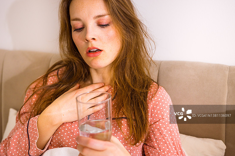 坐在床上，触摸喉咙，拿着一杯水的女人图片素材