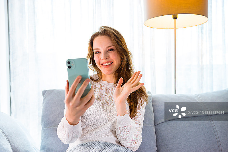 快乐的女人在沙发上用智能手机视频通话图片素材