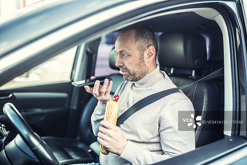 在车里手拿热狗用手机大声讲话的男人图片素材