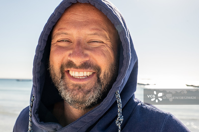 日出时分海滩上戴兜帽的微笑男人肖像图片素材
