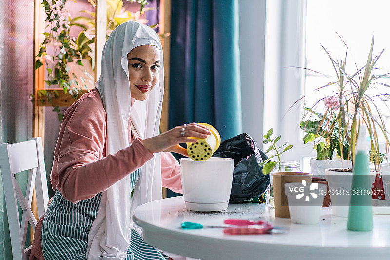 戴白色头巾的穆斯林女人在室内照料植物图片素材
