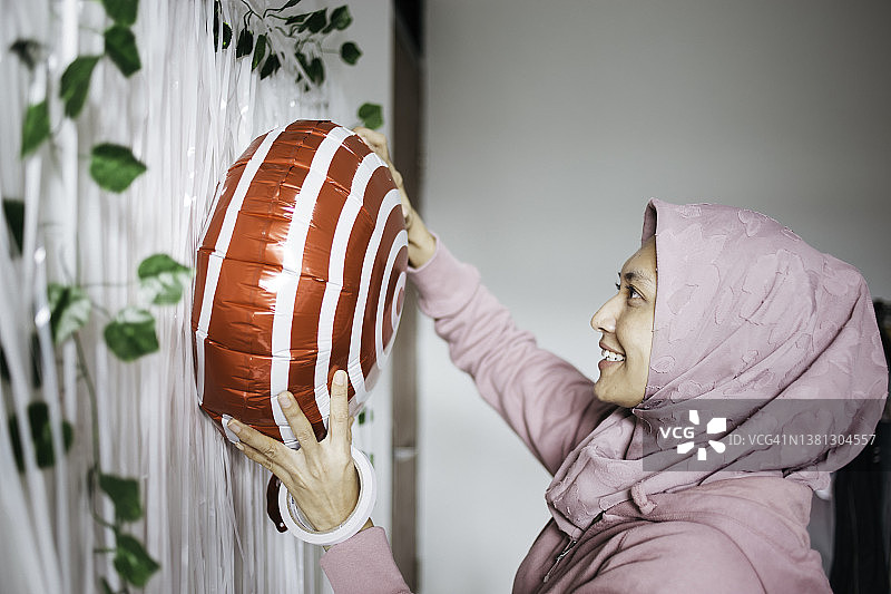 戴着头巾的年轻亚洲女性正在装饰，准备庆祝生日图片素材