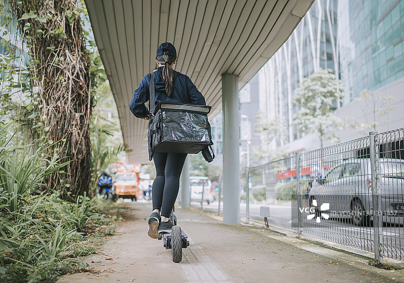 中国女送货员骑着电动滑板车在城市中运送货物图片素材