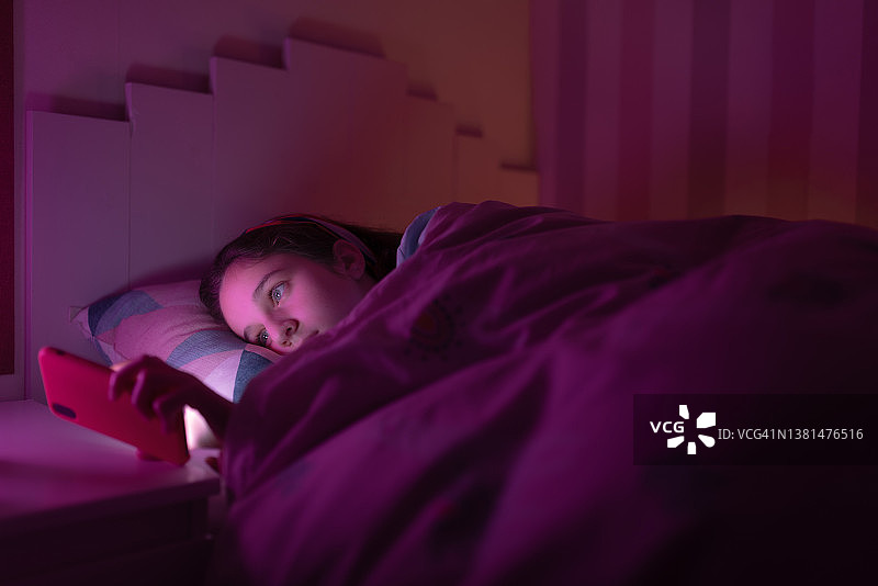 年轻女孩睡前用手机看东西的特写镜头图片素材