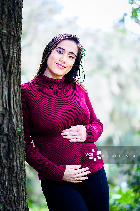 年轻漂亮的拉丁裔孕妇在风景优美的户外自然区幸福地抱着她怀孕3个月的肚子图片素材