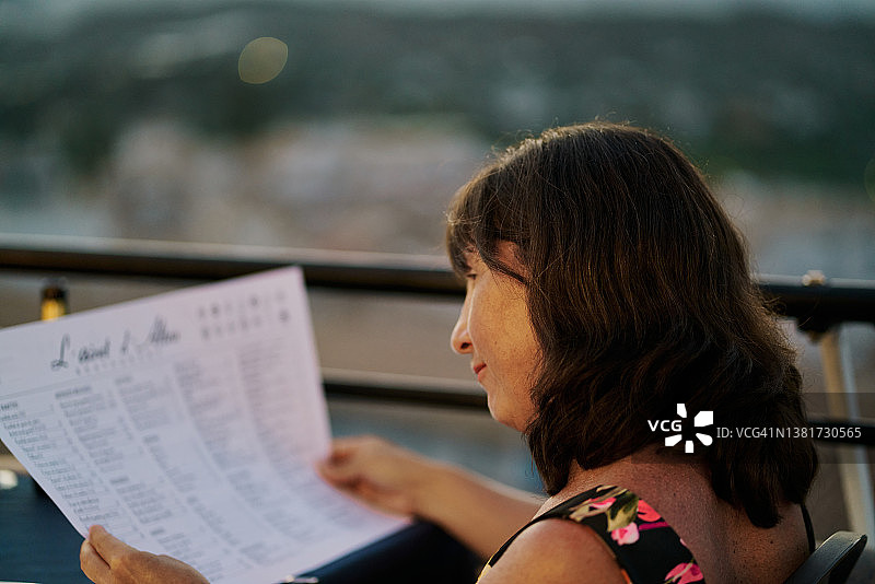 在日落时分的法国餐厅里坐在桌旁看菜单的女人图片素材