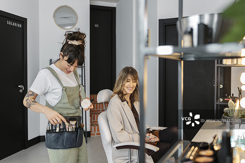 快乐的化妆师在沙龙里与坐在椅子上的顾客交谈图片素材