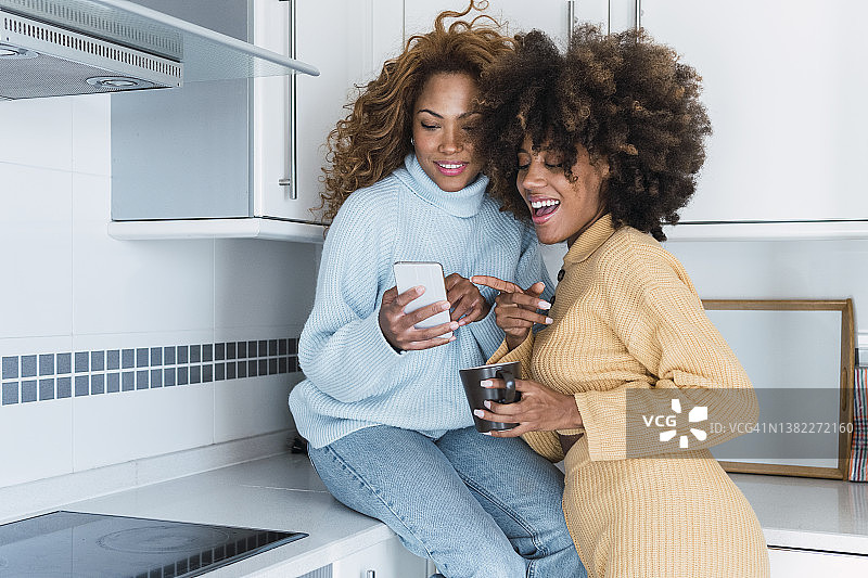 年轻女人在厨房与朋友分享手机图片素材