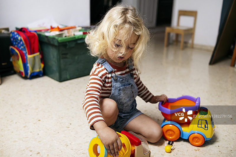 金发男孩在家里的地板上玩玩具车图片素材