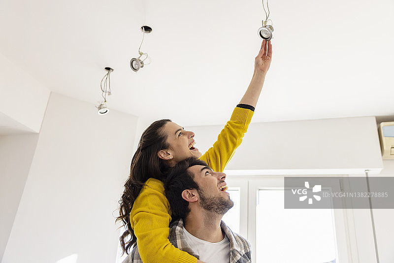 快乐的女人在新家里踩在男友背上更换灯泡图片素材