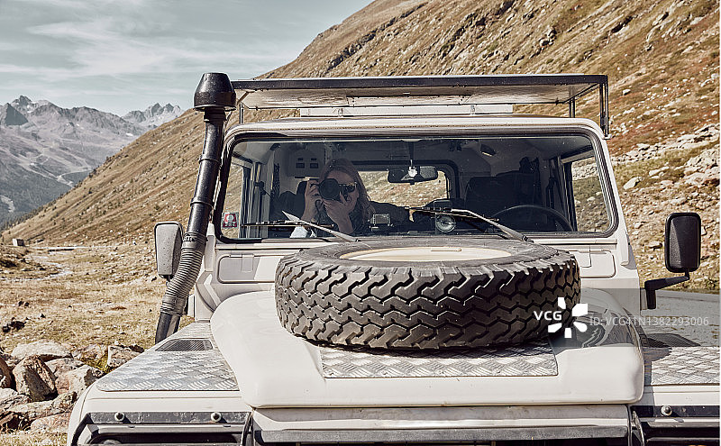 在厄茨塔尔阿尔卑斯山蒂梅尔斯约赫山口，透过越野车的挡风玻璃看到女人用相机拍摄图片素材