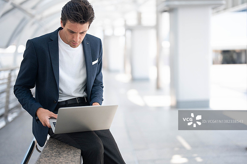 微笑的商人坐在楼梯上，戴着耳机使用手机和笔记本电脑图片素材