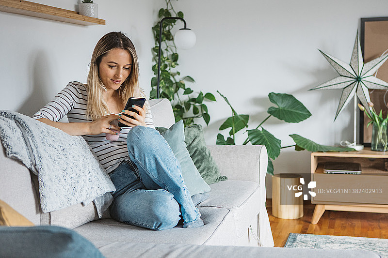 在家中沙发上使用手机的年轻女人图片素材