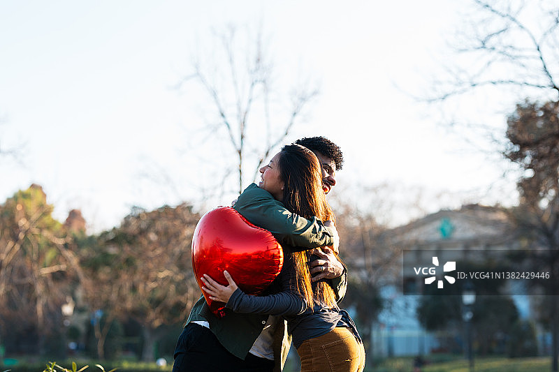 快乐的年轻人拥抱拿着心形红气球的爱人图片素材