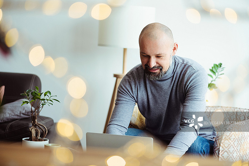 中年男人坐在客厅窗边使用笔记本电脑打字图片素材