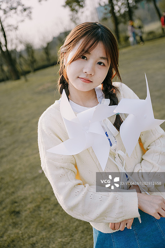 黄昏时草坪上拿着纸风车的亚洲女孩图片素材