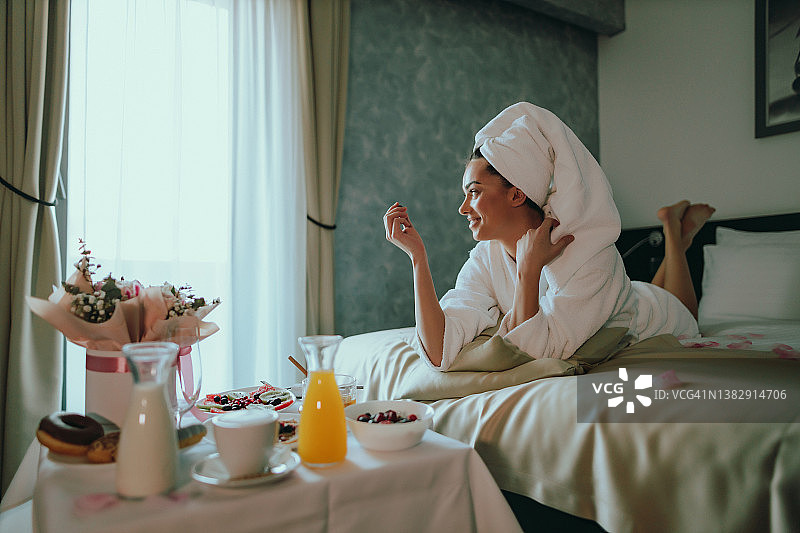 年轻女人在酒店房间的床上吃早餐图片素材