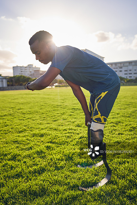 年轻的截肢运动员在阳光明媚的公园里查看智能手表图片素材