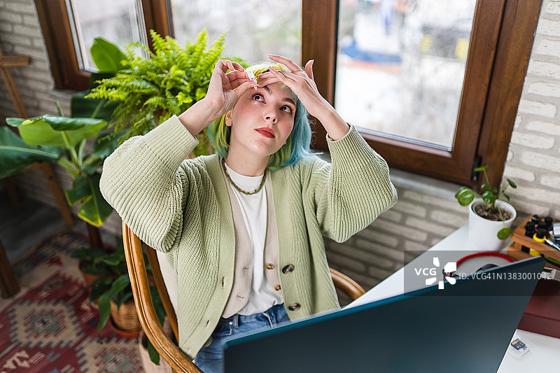 年轻女人工作时使用滴眼液缓解眼睛干涩图片素材