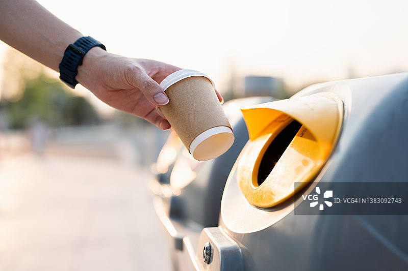 特写镜头：将空纸咖啡杯扔进回收箱图片素材