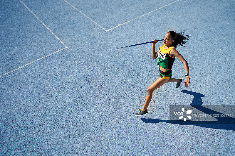 在阳光明媚的蓝色跑道上掷标枪的田径女运动员图片素材
