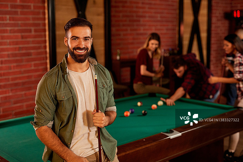 背景是朋友打台球的年轻男子肖像图片素材