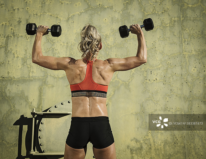 女子运动员用哑铃锻炼的后视图图片素材