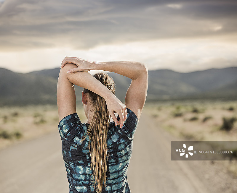 美国犹他州锡达堡，女子在沙漠景观的道路上伸展背部图片素材