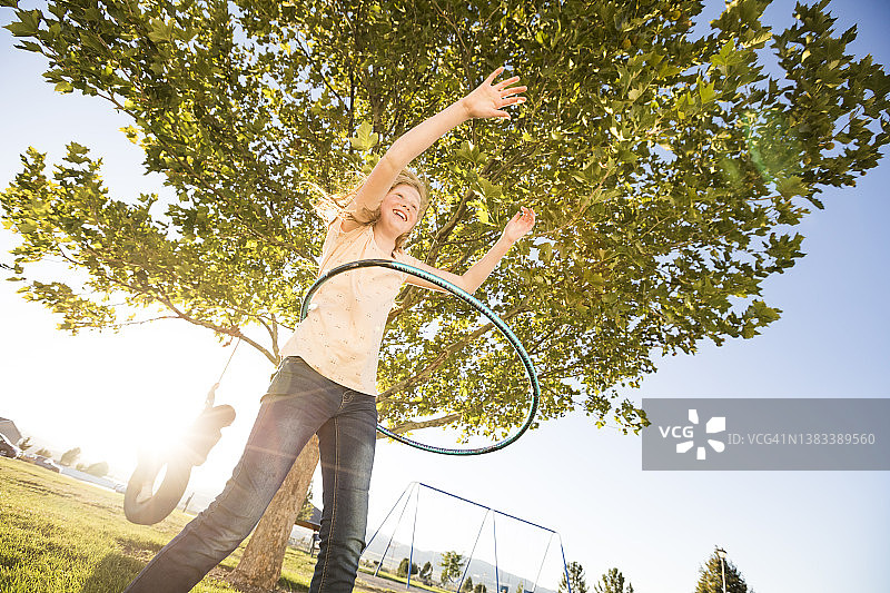 女孩（12-13岁）在玩呼啦圈，妹妹（10-11岁）在背景中的轮胎秋千上图片素材