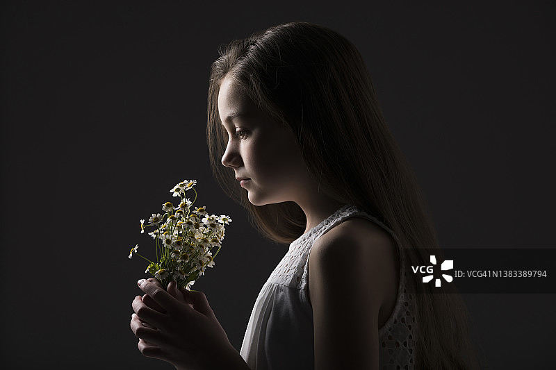 手捧野花的(10-11岁)女孩侧面像，黑色背景图片素材